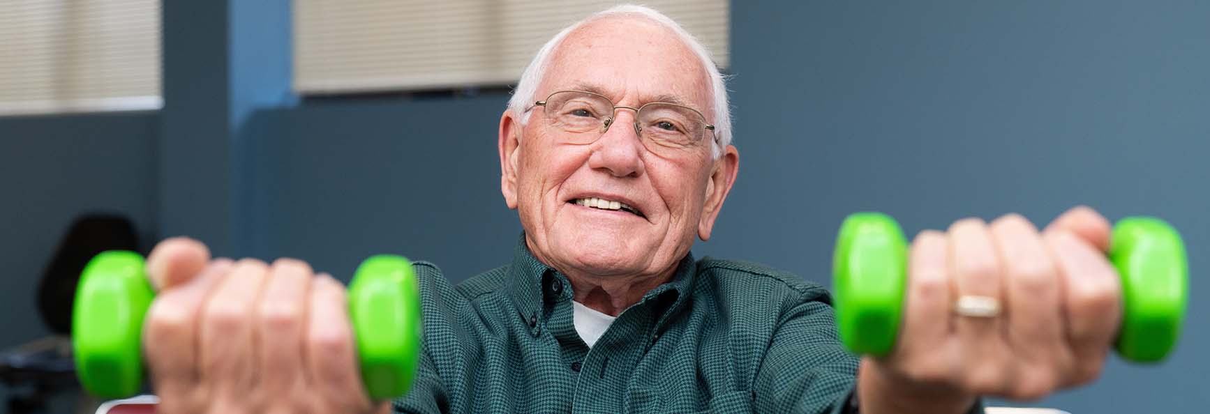 Smiling older male patient holing weights during a physical therapy session